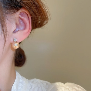 Detailed close-up of a zircon and champagne pearl earring worn on a model's ear
