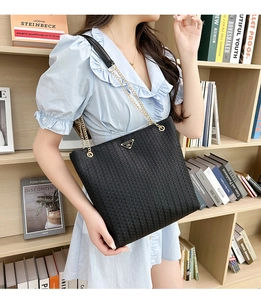 Detail of black woven texture tote bag with metal chain strap and triangular logo plate