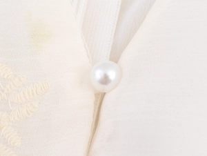Détail du bouton perle et de la broderie florale fine sur le tissu de robe blanc crème
