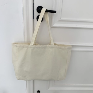 Detail of a beige large capacity canvas tote bag hanging on a white wooden door handle