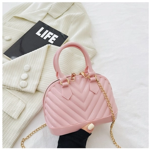 Pink jelly shell bag with gold chain strap held against a lifestyle background