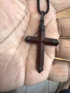 Vue détaillée d'un pendentif en croix de bois avec embouts métalliques à la main