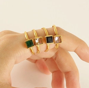 Detailed view of four colorful square gemstone rings in gold plating on model's hand