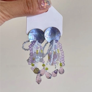 Détail de boucles d'oreilles à pompons violets avec perles et breloques en cristal