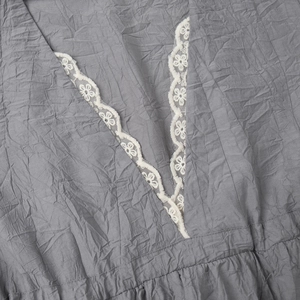Détail du col en V avec dentelle florale blanche et texture plissée sur robe grise