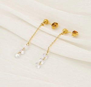 Close-up of gold long tassel earrings with clear crystal beads on white silk background
