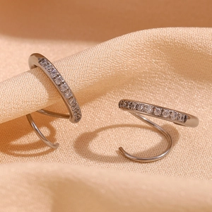 Gros plan de boucles d'oreilles spirales argentées serties de zircons sur tissu beige