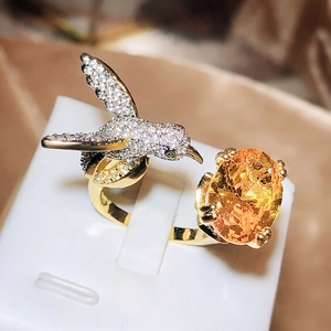 Macro detail of hummingbird ring with orange gemstone and crystal pavé setting
