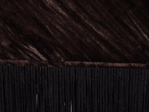 Detail of dark brown velvet fabric featuring fine black fringe tassels and pleated texture