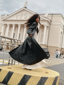 Detail of a black leather coat with lace-trim white dress against European architecture