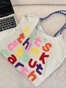 Green canvas tote bag with colorful towel embroidery and blue rope handles on a white rug