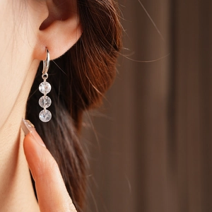 Detailed view of silver hook earrings with three vertical zircon stones on model