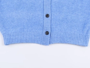 Dettaglio dell'orlo del cardigan azzurro con bottoni marroni e trama a costine