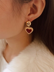 Close-up of heart-shaped gold enamel earrings on model with white faux fur outfit