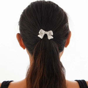 Detail showing a silver metal bow hair tie with radial textured lines on a ponytail