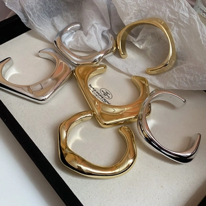 Close-up of irregular wavy gold and silver minimalist bangles on a textured display