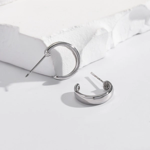 Minimalist silver C-shaped stud earrings in polished copper on a white stone base