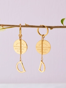 Détail de boucles d'oreilles dorées 18K avec breloque ronde et pendentif D sur bois