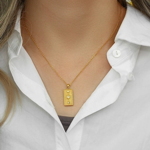 Gold rectangular sun tarot necklace with three cubic zirconia stones on white shirt