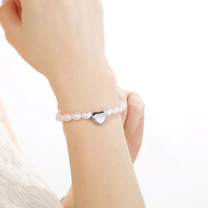French luxury style faux pearl bracelet with silver heart pendant on model's wrist