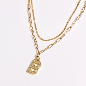Close-up of golden layered necklace with paperclip chain and zircon letter B pendant