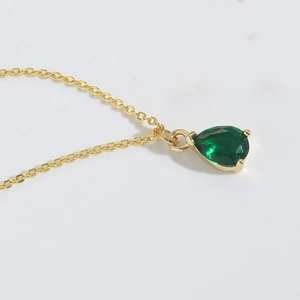 Macro shot of gold necklace with a pear-cut green gemstone pendant on white background