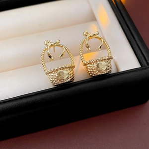 Detailed macro shot of golden bow basket earrings inside a black and white jewelry box