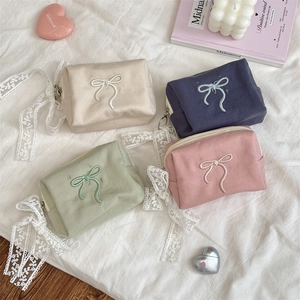 Flat lay of canvas cosmetic bags with bow embroidery in four pastel colors on lace fabric