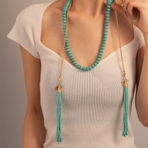 Détail d'un long collier ethnique avec perles turquoise, chaîne dorée et pendentif gland