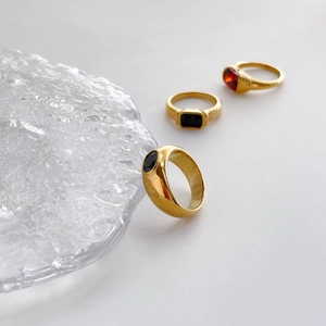 Close-up of gold rings set with black agate and red ruby stones on a textured background