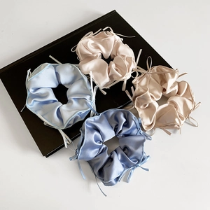 Set of four satin scrunchies with ribbons in blue and champagne on a black book