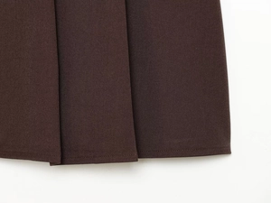 Détail de la jupe plissée marron foncé montrant le tissu en sergé et les coutures