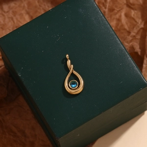 Detail of 18K gold teardrop pendant with blue gemstone on a luxury green jewelry box