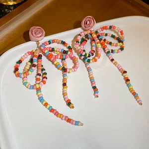 Detail of floral drop earrings featuring rainbow crystal beads and a pink fabric rose