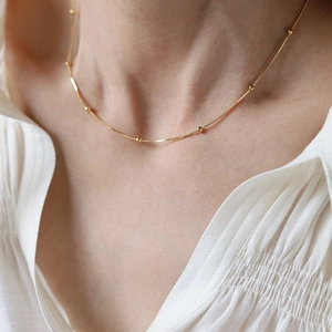 Close-up of golden snake bone chain necklace with small round beads on a female neck