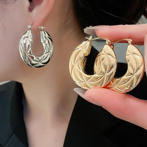 Detail of quilted hoop earrings in gold and silver finish with textured metal design