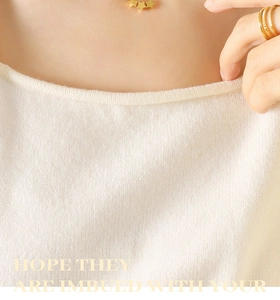 Détail d'un collier étoile sur un pull en maille crème avec une finition à col rond