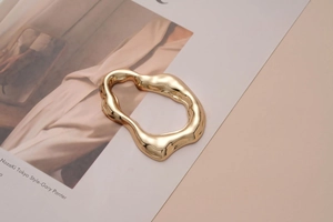 Close-up of a polished gold irregular metal buckle accessory on a fashion magazine