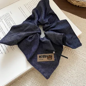 Blue denim bow hair scrunchie with leather patch on vintage book and knit backdrop