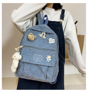 Detalle de mochila de pana azul claro con osito de peluche y pines decorativos