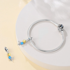 Detailed close-up of astronaut pendant with yellow and blue enamel spheres on silver bracelet