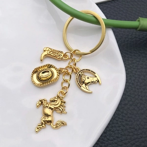 Golden western cowboy keychain set with horse, boot, hat and horseshoe charms on white tray