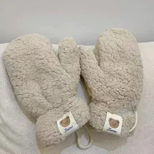 Detail of beige fleece mittens with cute bear patch and hanging lanyard for winter warmth