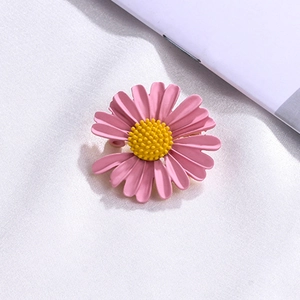 Macro detail of the pink enamel daisy brooch with a textured yellow center on white fabric