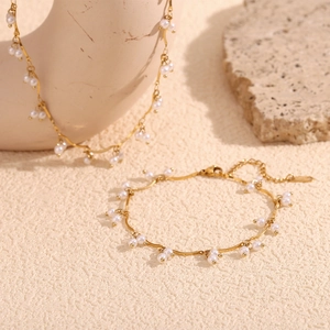 Detail of 18K gold plated chain necklace set with white pearls on a textured background