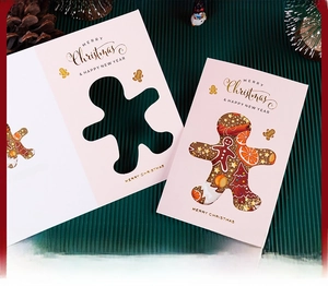 Close-up of pink Christmas card with gold foil text and gingerbread man cutout detail