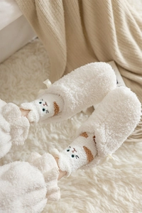 Detail of white plush socks with cat embroidery and a cute bow tie on a cozy background