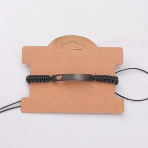 Detail of adjustable black woven rope bracelet with heart cutout metal bar on card