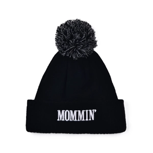 Black knit beanie with MOMMIN embroidery and a fluffy pom pom on white background
