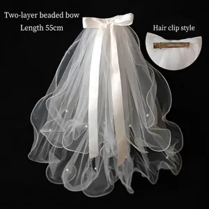 Detail of double-layer white bridal veil with pearls, silk bow, and a metal hair clip